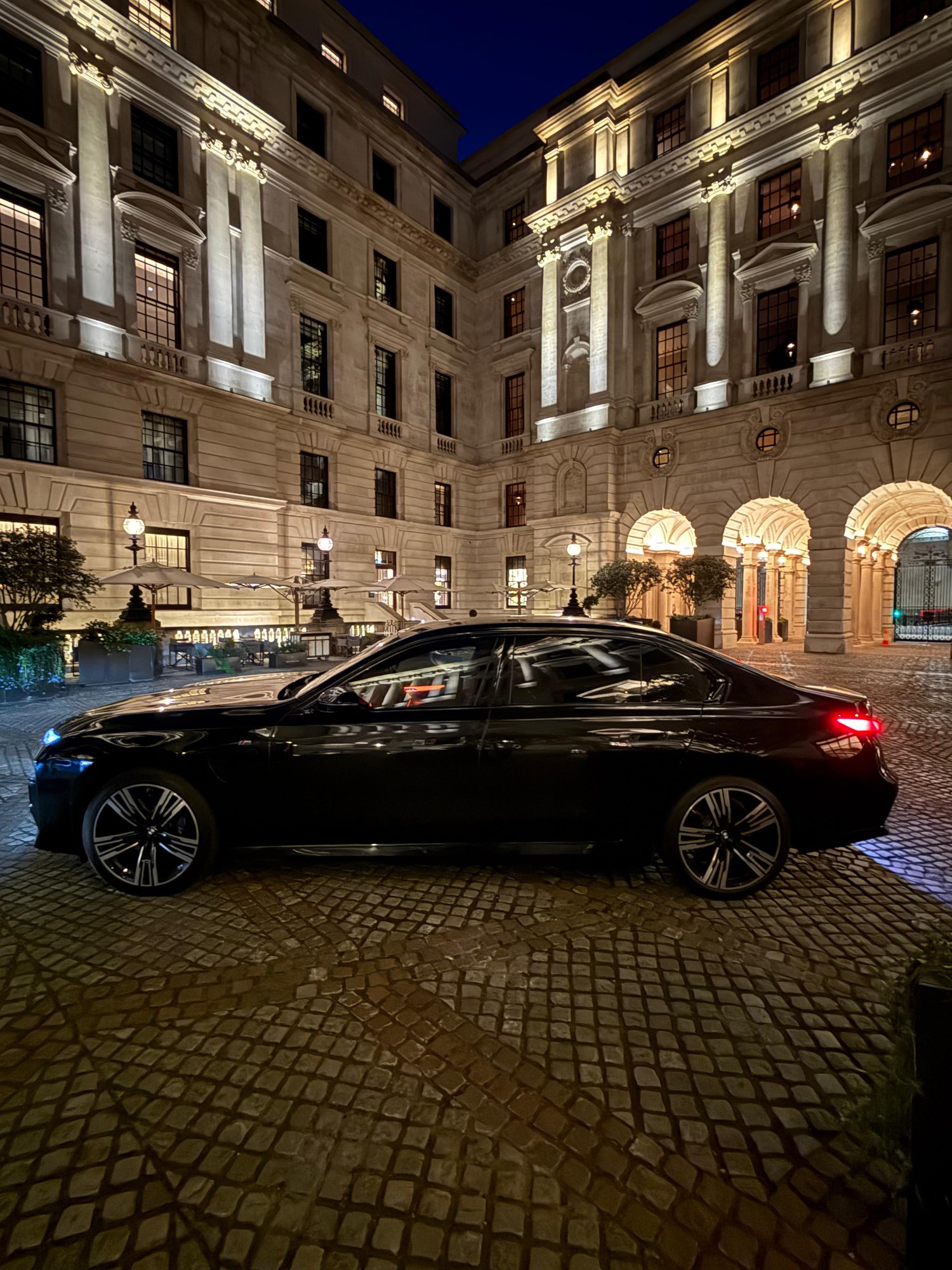 Black BMW 7 Series passing through a London courtyard at night